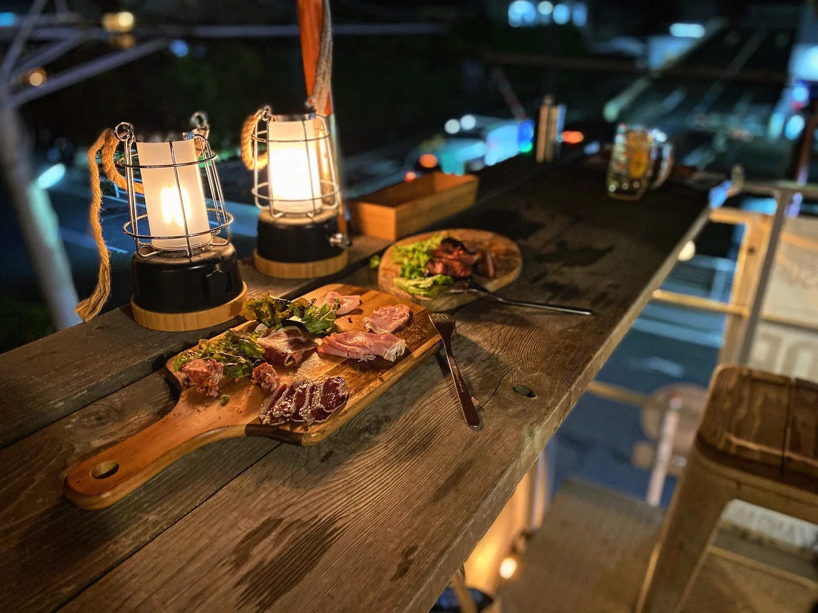 ランタンの明かりの下、木のボードと料理が並ぶ屋外の食卓。